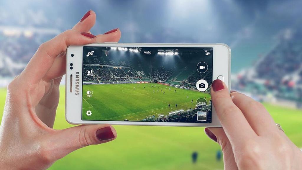 Deux mains tenant un iPhone durant un match de football… et terrain vue à travers l'écran du téléphone portable