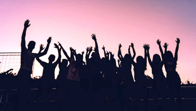 Photo en contrejour et coucher de soleil montrant un ensemble de personnes avec les bras conjointement levés vers le ciel