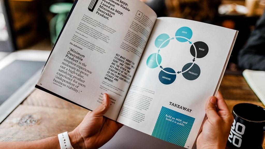 Photo montrant 2 mains tenant un livre ouvert avec à droite un schéma représentant les différentes étapes du lean management