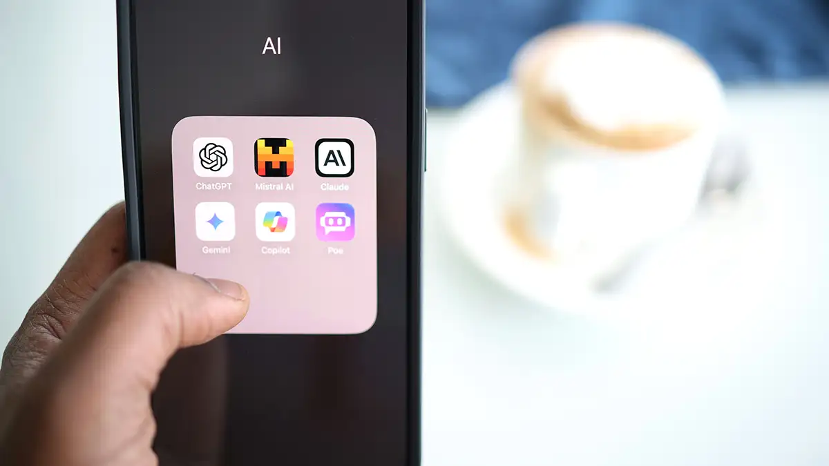 Main à gauche de l'image tenant un Iphone avec les icônes des assistants IA : Claude, Mistral, ChatGPT